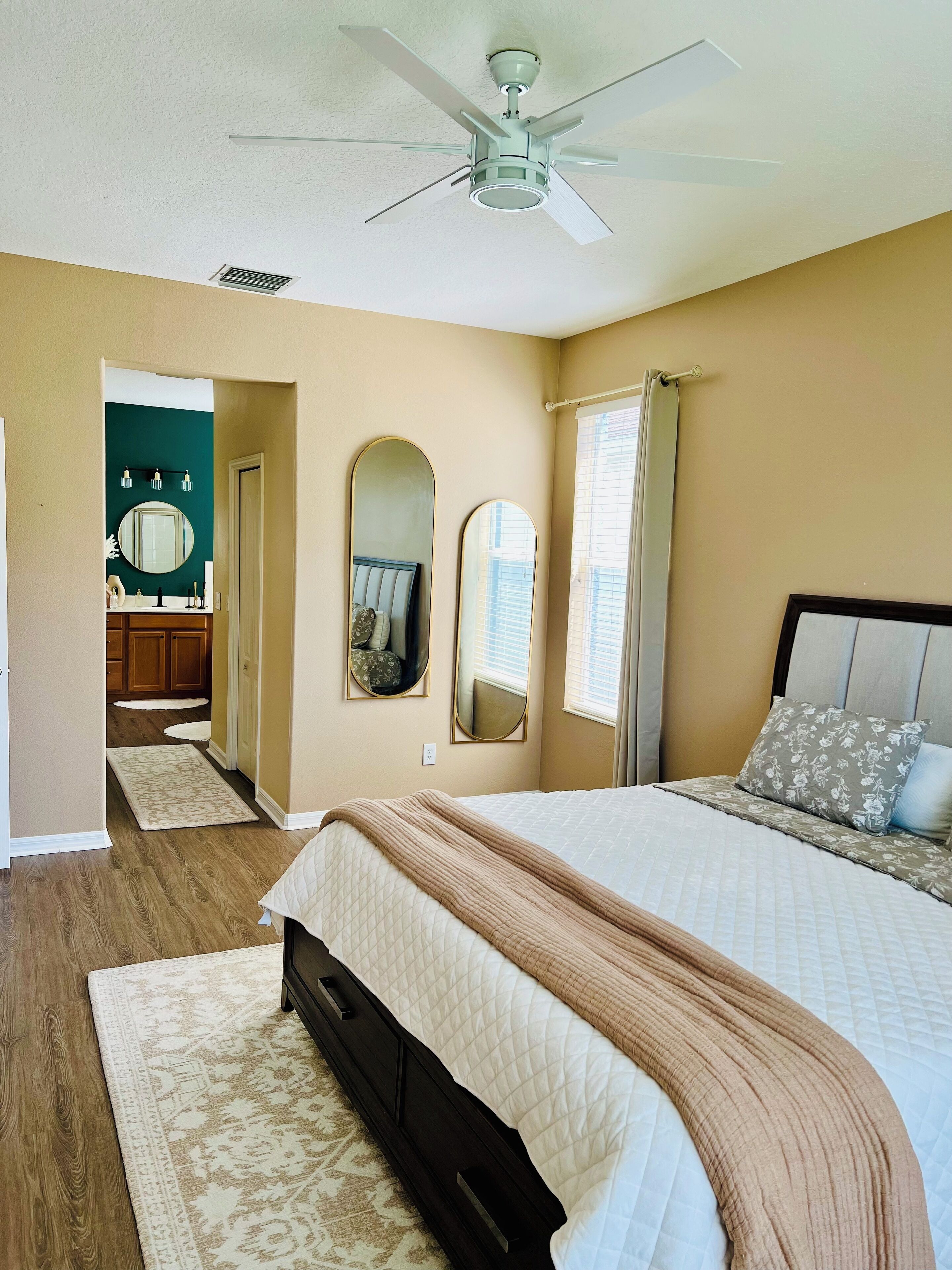 A bedroom with a bed, a ceiling fan, a large mirror, and a bathroom visible through an open door.