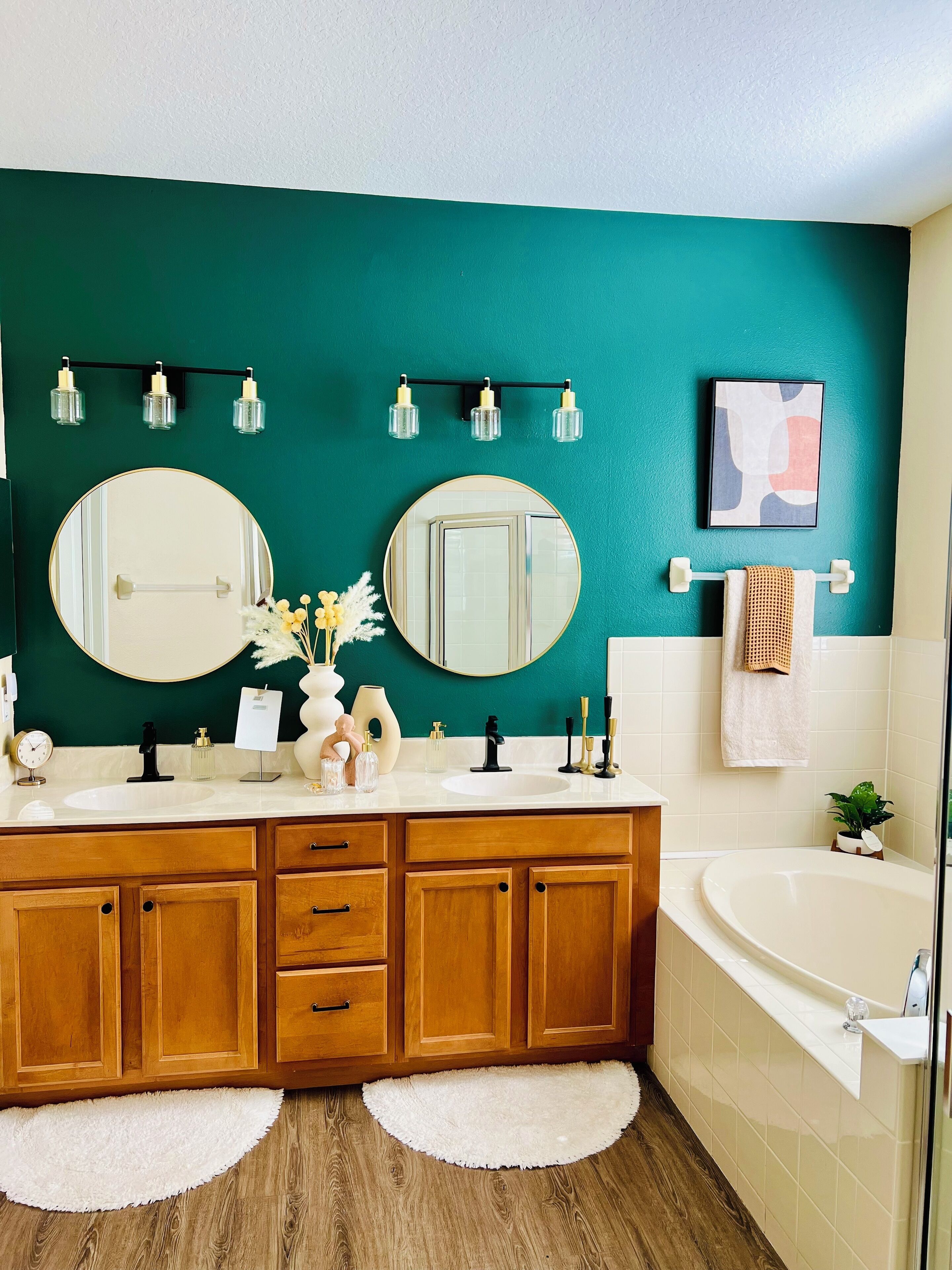 A modern bathroom with two large mirrors, a white sink, wooden cabinets, a bathtub, and teal walls.