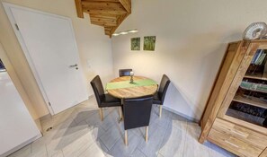Ein Essbereich mit einem runden Tisch, vier Stühlen, einem Holzschrank mit Glastüren und zwei Wandleuchten.