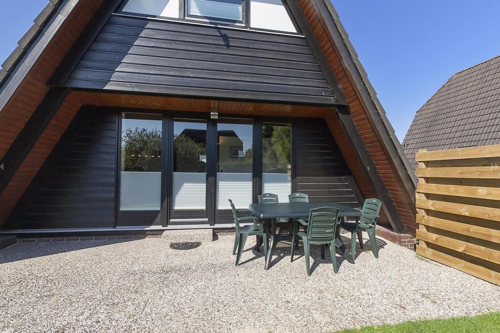 A modern building with a sloped roof, large windows, and a patio area with a table and chairs.