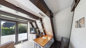 Ett modernt sovrum i loftstil med ett stort fönster, ett matbord i trä och en tv.