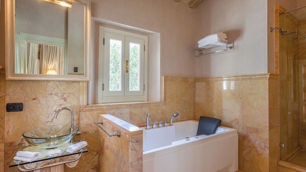 Un baño con un lavabo de cristal, una bañera blanca, un espejo y una ventana.