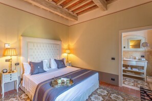 Habitación de hotel con una cama grande, dos mesitas de noche con lámparas, una bandeja con artículos de desayuno y un baño con espejo y lavamanos.