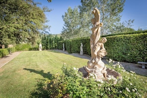 Un jardín con estatuas, césped bien cuidado y setos.