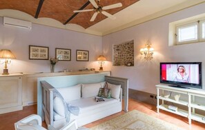 A living room with a white sofa, a television on a white stand, a ceiling fan, and a stone wall.