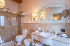 A bathroom with a glass-enclosed shower, a toilet, a bidet, a sink with a mirror, and toiletries.