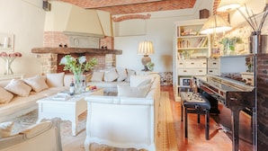 Una sala de estar acogedora con chimenea, asientos cómodos, un piano y una estantería.