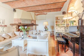 A cozy living room with a fireplace, comfortable seating, a piano, and a bookshelf.