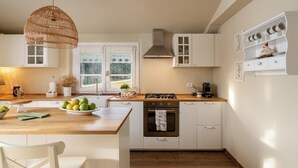 Uma cozinha moderna com armários brancos, bancada de madeira, fogão a gás e luminária de vime suspensa.