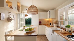 Uma cozinha moderna com armários brancos, bancada de madeira, luminária pendente e vista para o jardim.