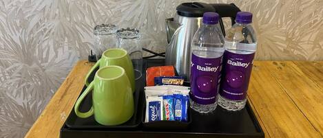 A tray with green mugs, Bailey's water bottles, and coffee packets on a wooden table.
