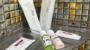 Ein Badezimmer mit gefliesten Wänden, einem Waschbecken aus Glas und Pflegeprodukten, darunter eine Shampooflasche, Körperlotion und eine Seife.