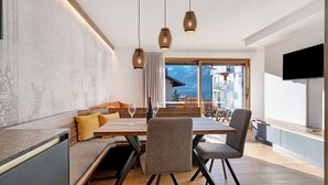 A modern dining area with a wooden table, grey upholstered chairs, and hanging pendant lights. - Apartment 'Villa Helena' with Mountain View, Private Terrace and Wi-Fi (Cavalese)