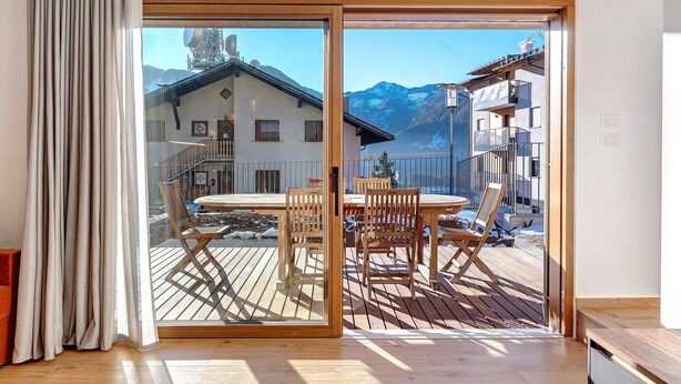 A room with a sliding glass door leading to a wooden deck with outdoor furniture, a mountain view, and a modern interior. - Apartment 'Villa Helena' with Mountain View, Private Terrace and Wi-Fi (Cavalese)