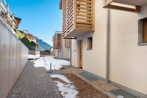 A narrow alleyway with buildings on either side, a paved walkway, and a snow-covered ground.