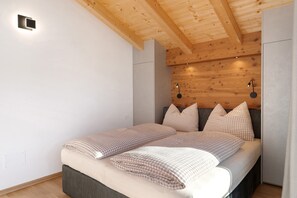 A bedroom with a wooden ceiling, a bed with checkered bedding, and two wall-mounted lights.