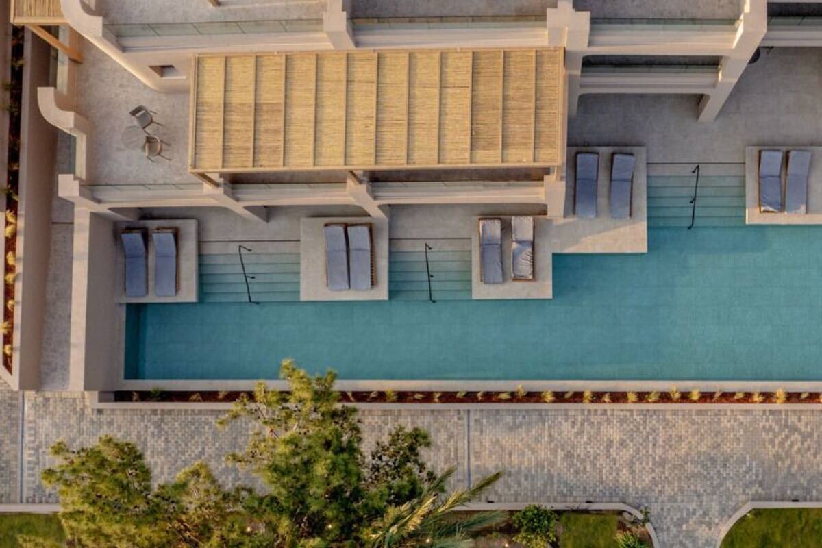 An aerial view of a hotel with a swimming pool, multiple lounge areas, and a well-maintained garden.