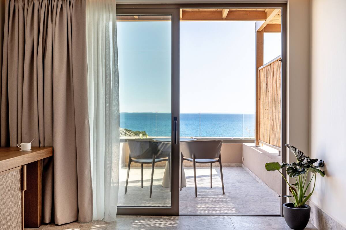A balcony with a view of the sea, a table with a cup, and a potted plant.