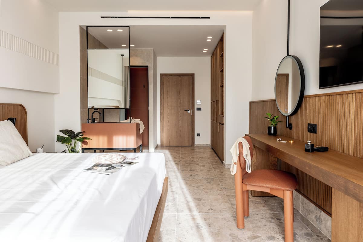 A modern hotel room with a bed, a wooden desk, a chair, a mirror, and a television.