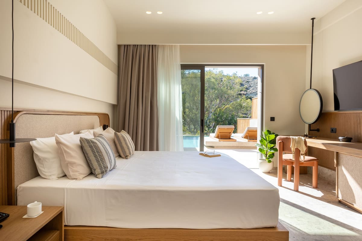 A modern hotel room with a large bed, a desk, a chair, a TV, and a view of the outdoors.