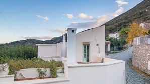 A white building with a stone pathway leading to a door, surrounded by greenery and hills. - Traditional Villa w/ Pool & BBQ, near Rethymno (Atsipades)