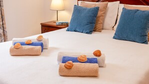 Una cama bien hecha con almohadas azules y color beige, un cabecero de madera y una mesita de noche con una lámpara y libros.