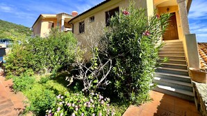 Ein Gebäude im mediterranen Stil mit einem Ziegeldach, einer Steintreppe, die zum Eingang führt, und einem Garten mit blühenden Pflanzen.