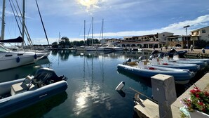 Ein Yachthafen mit verschiedenen vertäuten Booten, darunter Segelboote und Motorboote, und ein Gebäude mit einem Restaurant im Hintergrund.