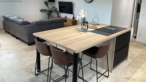 Une cuisine moderne avec un plan de travail en bois, des tabourets de bar, un téléviseur et un coin repas avec un canapé.
