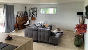 Un salon moderne avec un canapé d’angle gris, un piano en bois et un coin repas doté d’une table en bois.