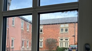Une fenêtre donnant sur un bâtiment en briques, une clôture et une voiture garée.