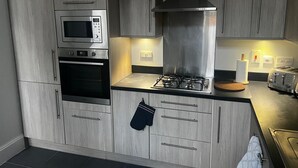 Une cuisine moderne avec des meubles de couleur grise, un micro-ondes encastré, un four et une cuisinière à gaz.