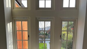 Une pièce dotée d’une grande fenêtre donnant sur un jardin, d’un canapé agrémenté de coussins à motifs et d’une petite table sur laquelle sont posées des bougies.