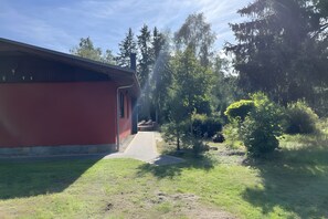 Een rood gebouw met een geplaveid pad dat naar een deur leidt, omgeven door groen en bomen.