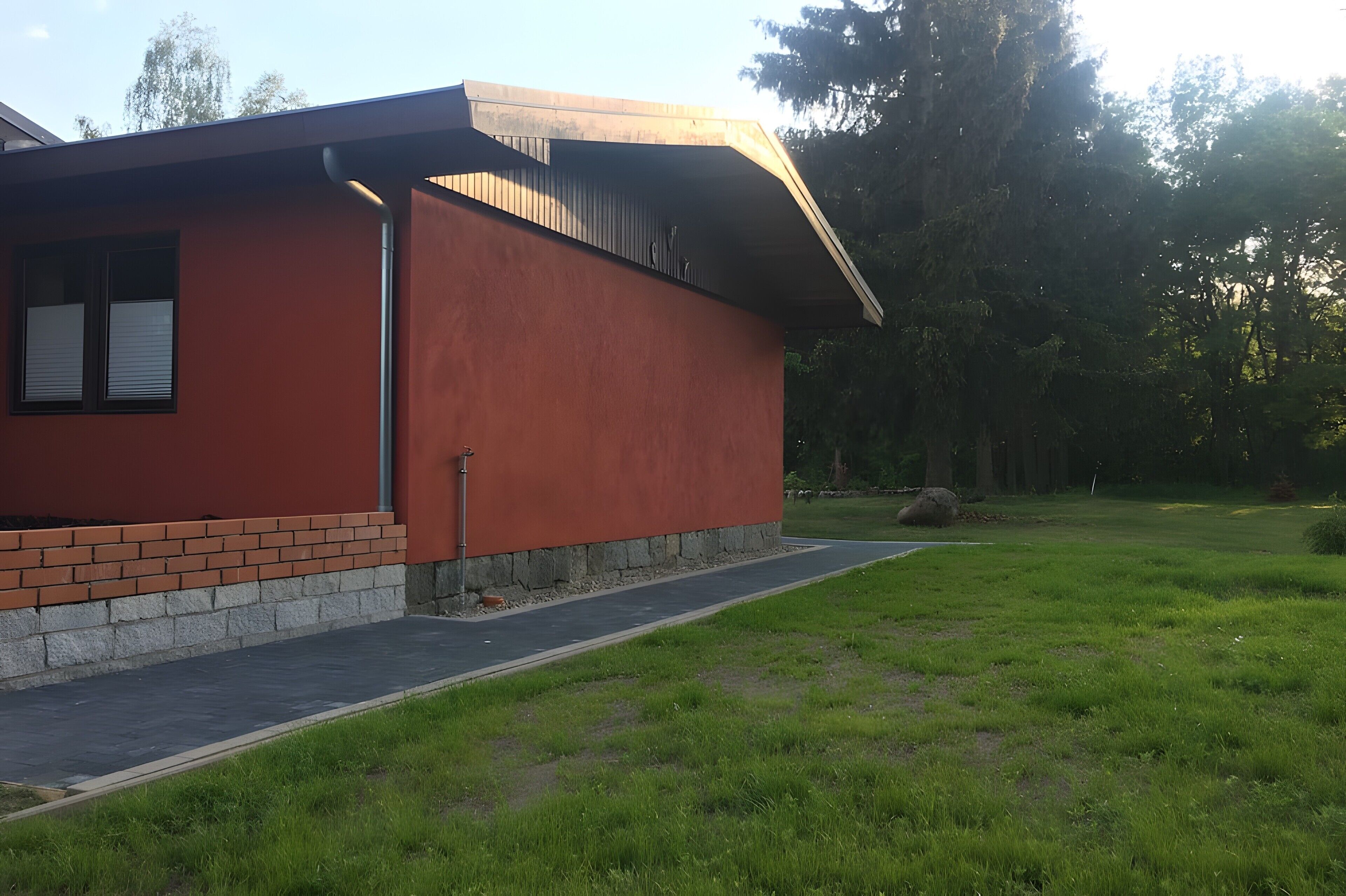 Un edificio moderno con base de ladrillo y fachada roja, rodeado de césped y árboles.