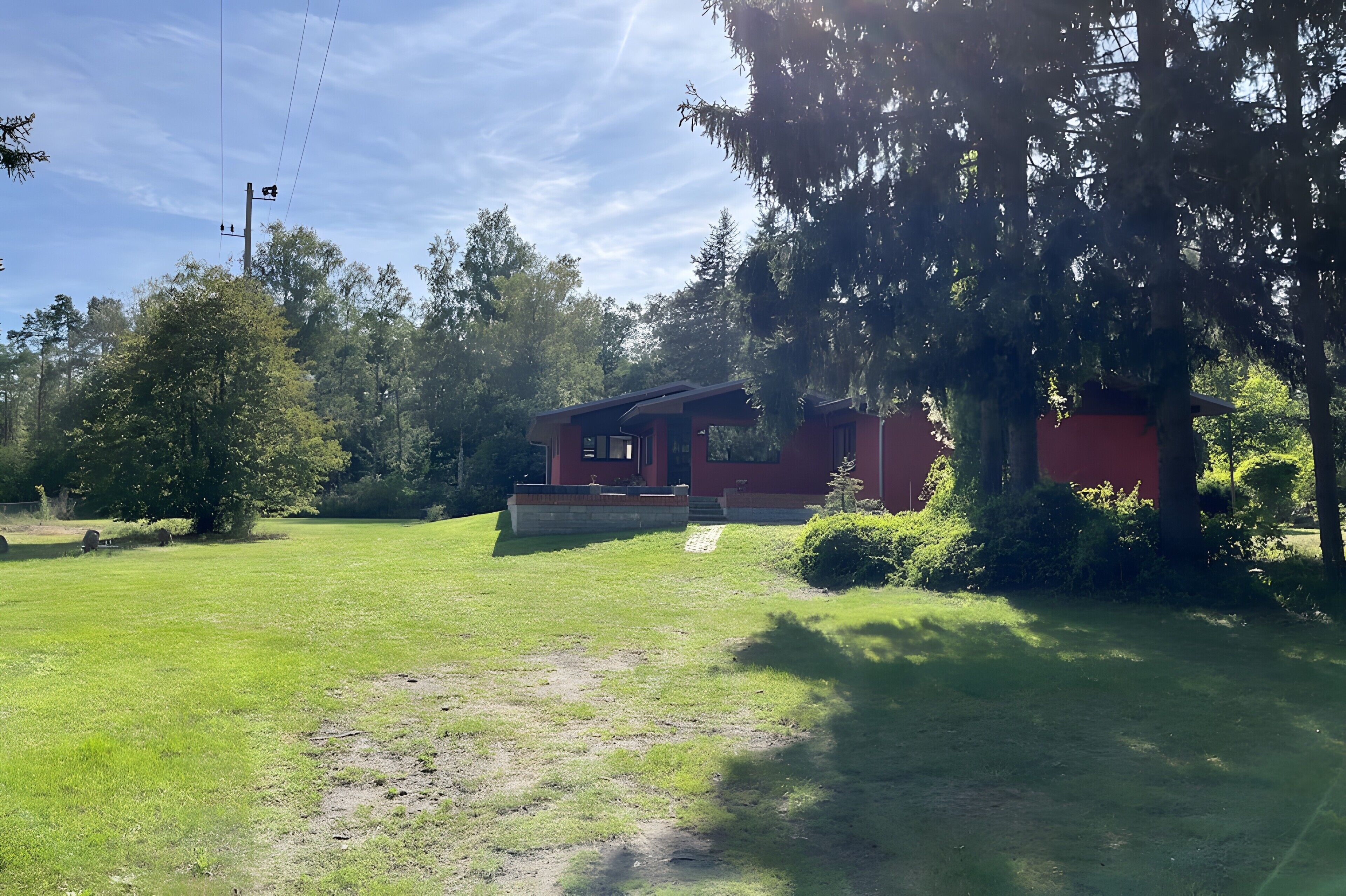 Um edifício vermelho com varanda coberta, cercado por um gramado e árvores.
