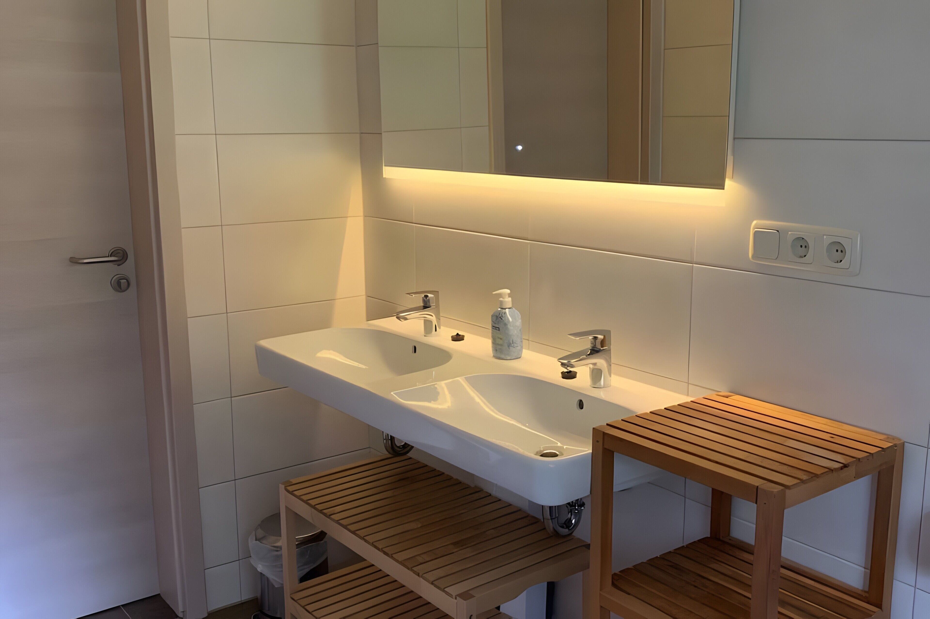 A modern bathroom with a double sink, a mirror, and a wooden shelf.