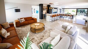 A modern living room with a brown leather sofa, a white sofa, and a wooden coffee table. There is a kitchen area with a bar and chairs. - 1160 Nagel Langebaan Country Estate (Langebaan)