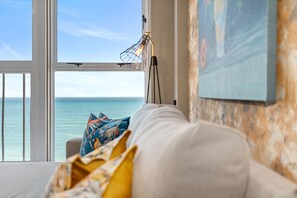Una habitación con vistas al mar, un sofá blanco con cojines de colores y una lámpara con pantalla de estructura metálica.