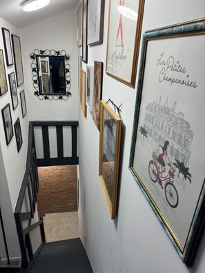 A hallway with a staircase, framed artwork, and a mirror. - Masion de ville Champenoise (Épernay)