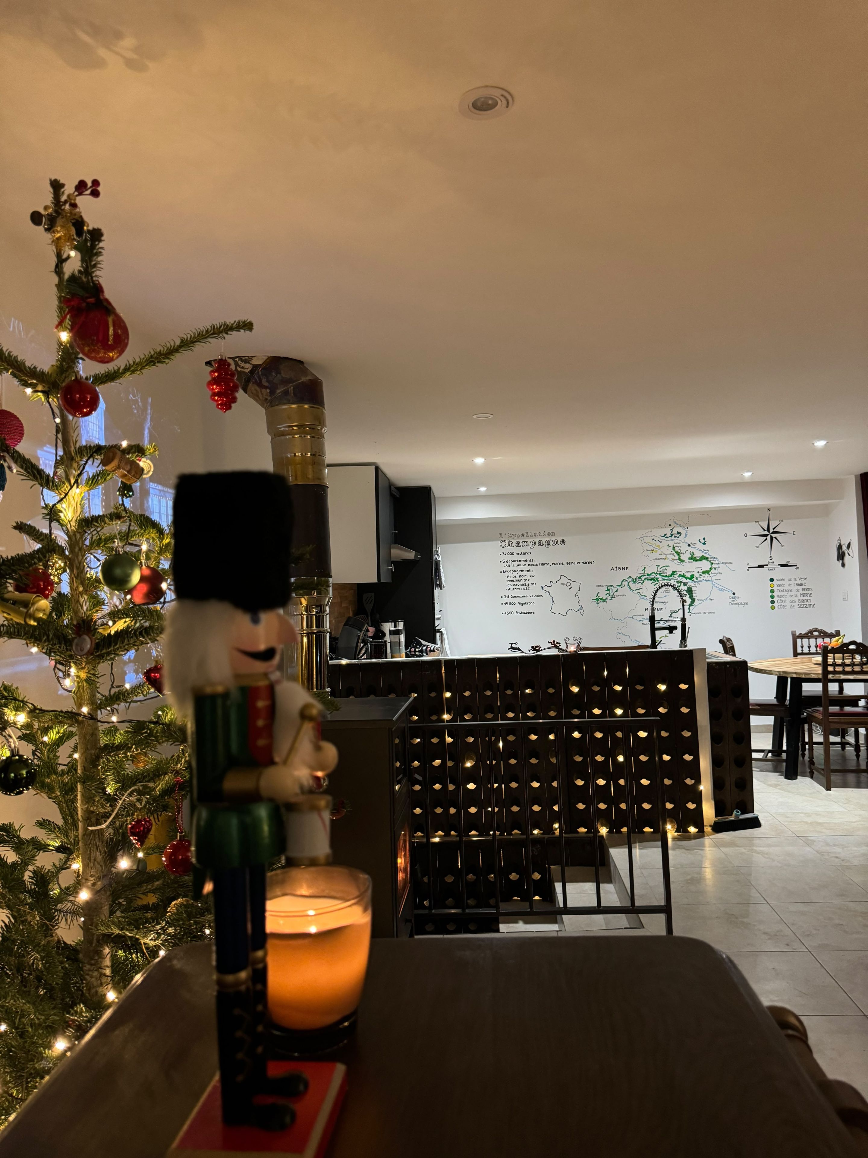 Un árbol de Navidad adornado con detalles y un soldado de hojalata, una vela encendida y una estantería para vinos en un interior moderno.