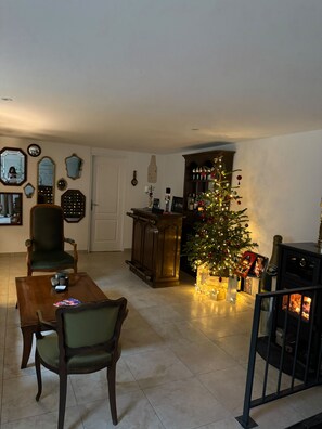 Un salon avec un sapin de Noël, une cheminée et un coin repas comprenant des chaises et une table.
