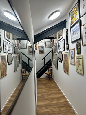 Un couloir avec un escalier, un plancher en bois et des murs ornés de tableaux et d’affiches encadrés.
