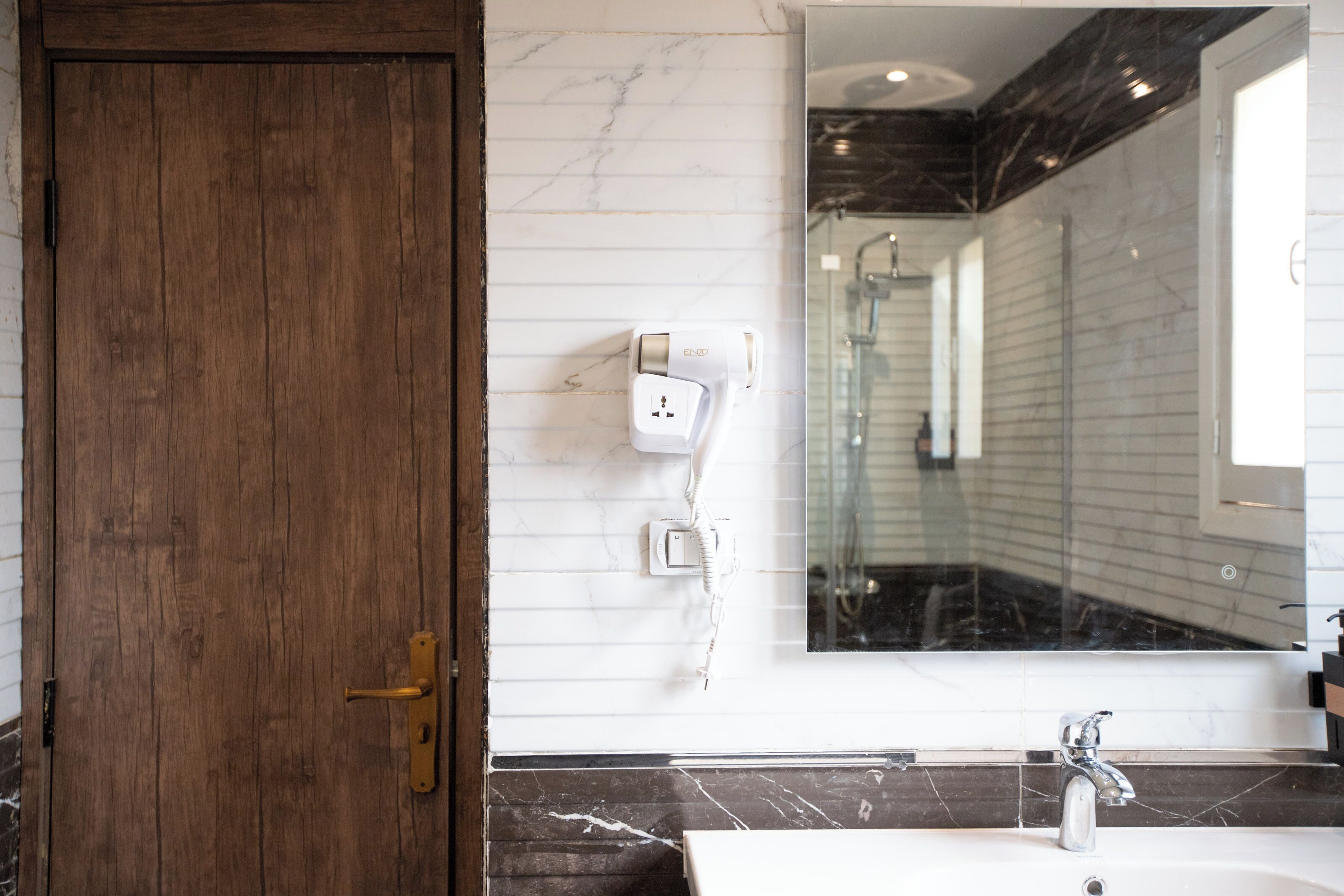 A bathroom with a wooden door, a white sink, a mirror, and a shower area.