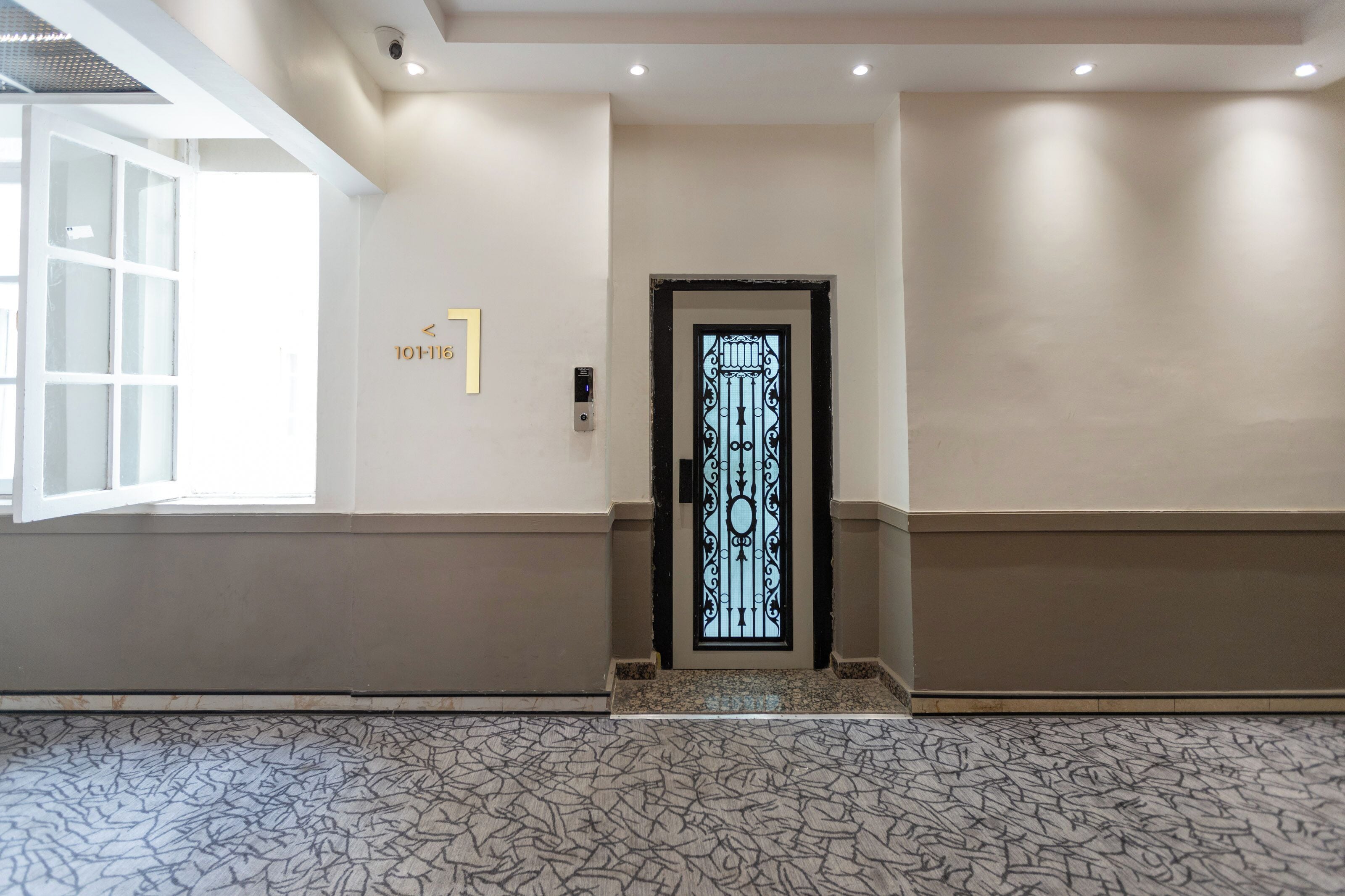 A hallway with a patterned floor, a door with a decorative glass panel, and a sign with numbers.