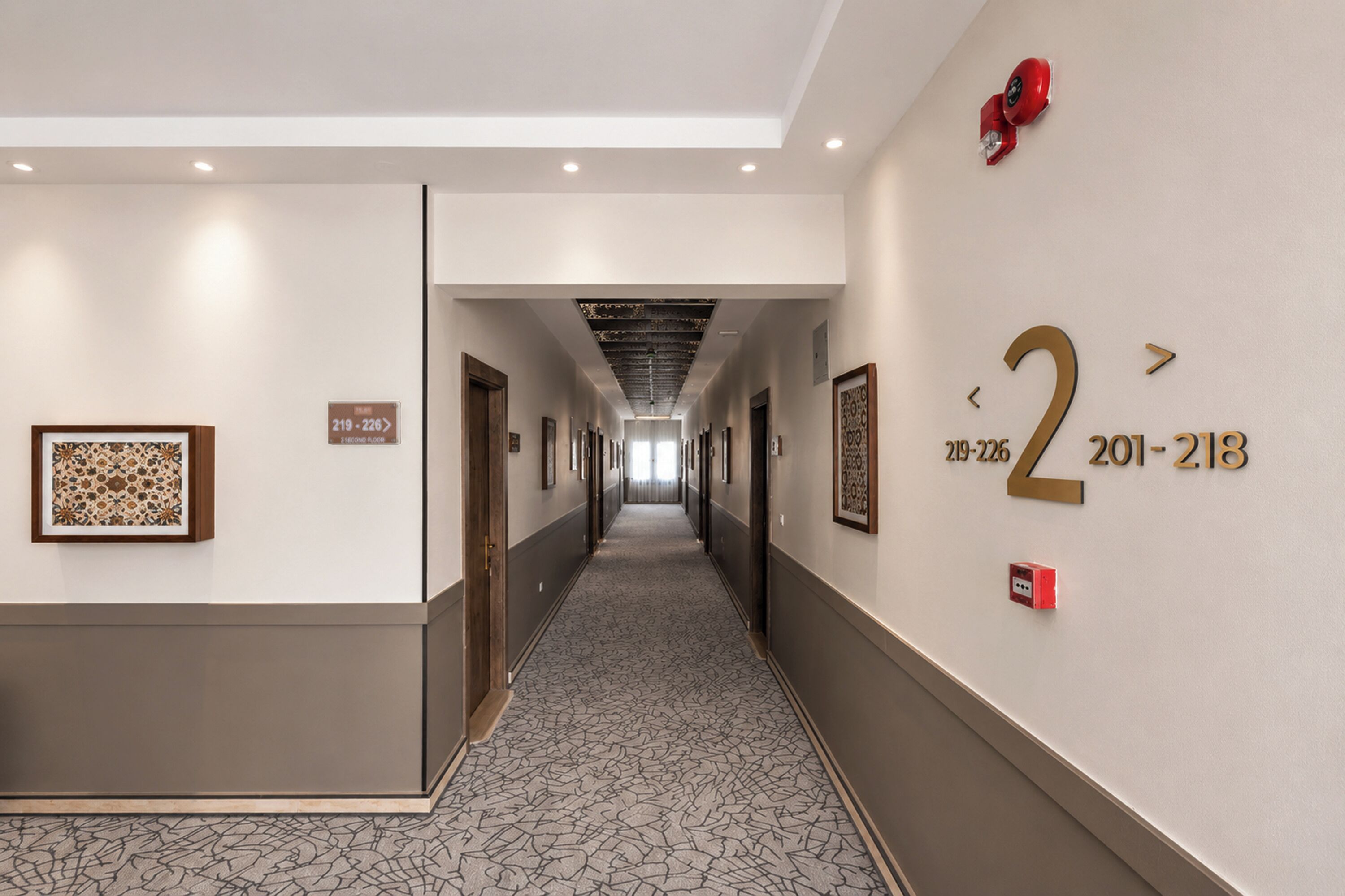 A hotel hallway with framed artwork, numbered doors, and a carpeted floor.