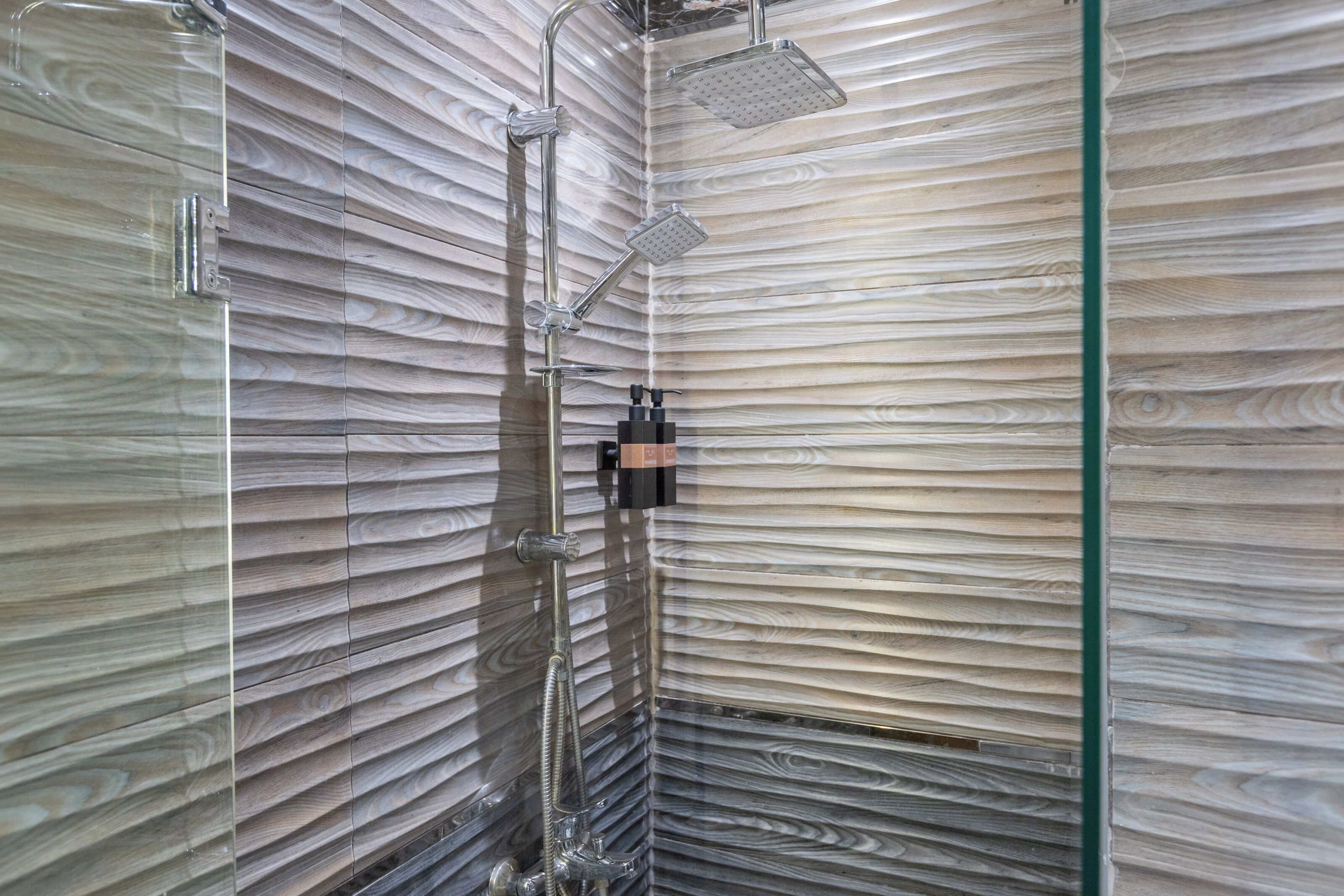 A shower with a glass enclosure, a handheld showerhead, and a wall-mounted control panel.