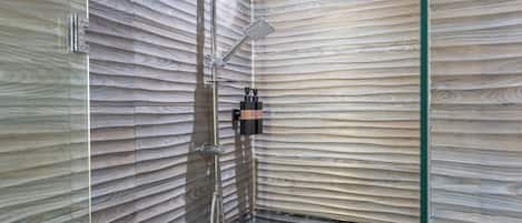Ducha con cerramiento de vidrio, cabezal de ducha manual y panel de control en la pared.