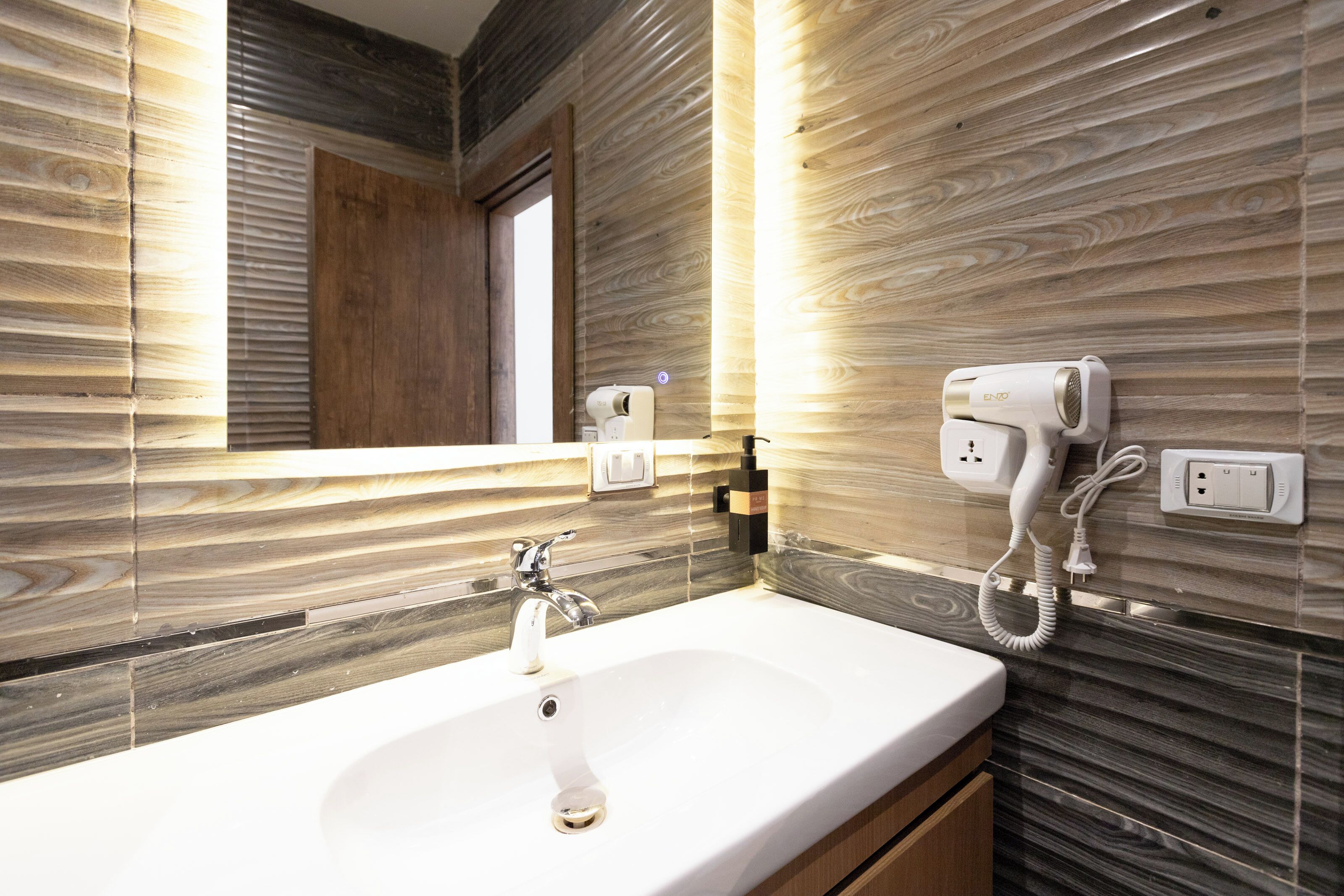 A bathroom with a sink, mirror, and hairdryer on a wall with wood-like paneling.