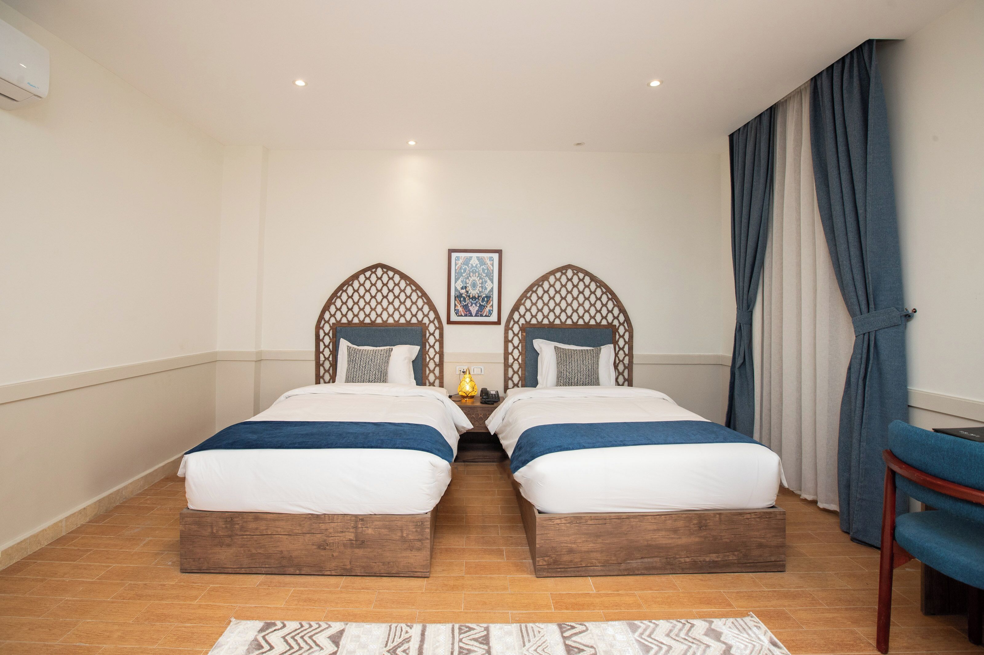 A hotel room with two beds, a wooden headboard, a nightstand, a lamp, and a chair.